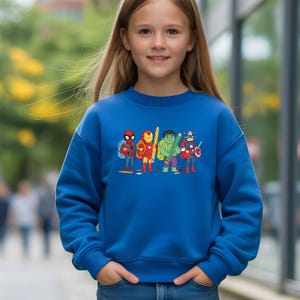 May include: A blue sweatshirt with a cartoon graphic of superheroes, including Spider-Man, Iron Man, Hulk, and Captain America, each holding pencils and backpacks. The sweatshirt is worn by a young person.