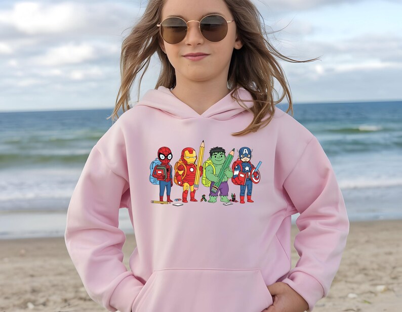 Puede incluir: Sudadera con capucha rosa claro con un dise&ntilde;o de dibujos animados de superh&eacute;roes como estudiantes. El dise&ntilde;o incluye a Spider-Man, Iron Man, Hulk y Capit&aacute;n Am&eacute;rica, cada uno con &uacute;tiles escolares. La sudadera tiene una capucha con cord&oacute;n.