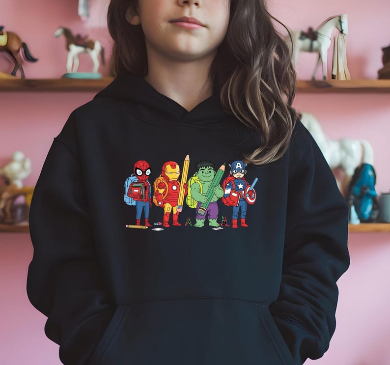 Puede incluir: Sudadera con capucha negra con un gr&aacute;fico colorido de superh&eacute;roes de Marvel como estudiantes, cada uno sosteniendo un l&aacute;piz o &uacute;tiles escolares. Los personajes incluyen a Spider-Man, Iron Man, Hulk y Capit&aacute;n Am&eacute;rica. Un dise&ntilde;o divertido de los Vengadores.