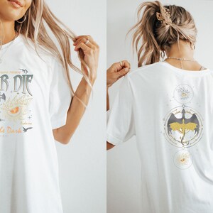 Puede incluir: Camiseta blanca con un estampado gr&aacute;fico de un drag&oacute;n y el texto "Fly or Die" y "Brave the Dark". La parte posterior de la camiseta tiene un estampado gr&aacute;fico de un drag&oacute;n con un c&iacute;rculo alrededor.