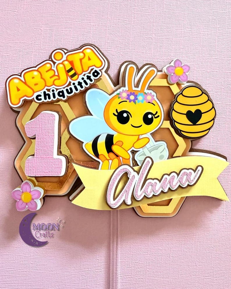 Puede incluir: Adorno de pastel en capas con una abeja de dibujos animados con una corona de flores, un dise&ntilde;o de panal y el nombre "Alana". El adorno incluye el texto "Abeja Chiquitita" y el n&uacute;mero "1", con detalles en rosa y amarillo.