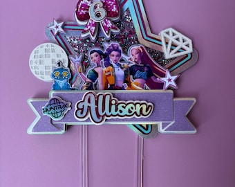 May include: A cake topper with a purple banner that reads "Allison" in a script font. The topper features a bow with the number "6", three cartoon characters, and a diamond shape. The topper is on a purple background.