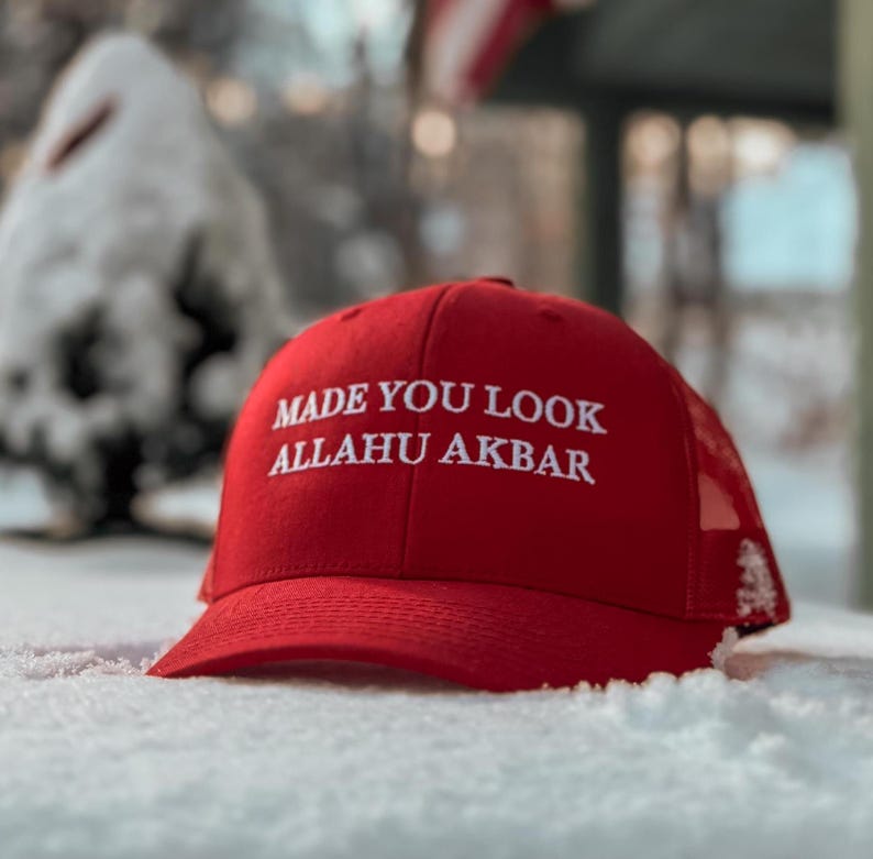 May include: Red baseball cap with a white mesh back. The cap has white embroidered text that reads "Made You Look Allahu Akbar".