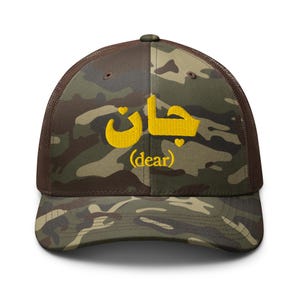 Puede incluir: Una gorra de camionero de camuflaje con la palabra árabe "Habibi" bordada en amarillo, que significa "querido" en español.
