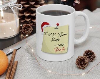 May include: A white ceramic mug featuring a graphic of a yellow sticky note pinned to the surface. The note displays the text F@*K Them Kids - xoxo Santa in black and red script, accented by a small red Santa hat on the top left corner.