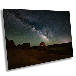 May include: A large, natural sandstone arch stands silhouetted against a dark night sky filled with stars and the Milky Way galaxy.