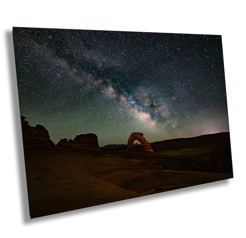 May include: A large, natural sandstone arch stands silhouetted against a dark night sky filled with stars and the Milky Way galaxy.