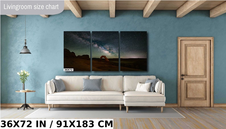 May include: A three-panel canvas print of a starry night sky with the Milky Way galaxy over a red rock arch. The print is 36 inches by 72 inches and is displayed on a white sectional sofa in a living room with a blue wall.