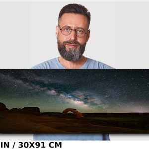 May include: A night sky photograph featuring the Milky Way galaxy over a desert landscape with a natural sandstone arch. The image is 12x36 inches or 30x91 centimeters.