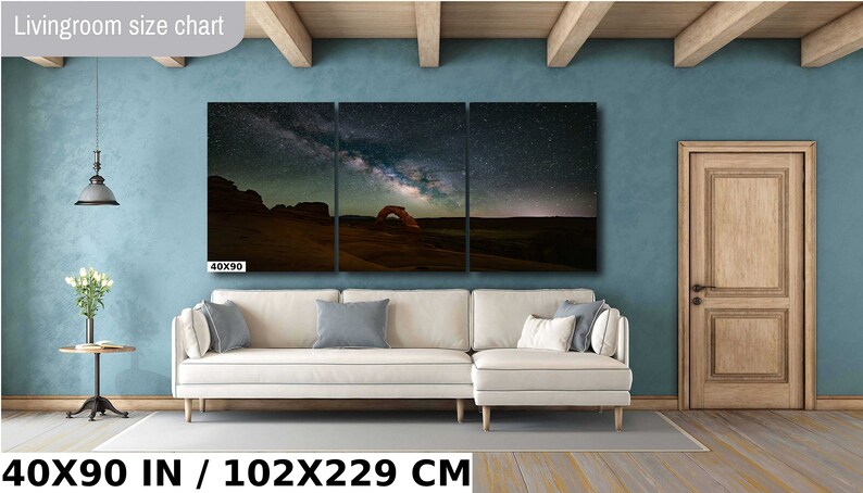 May include: A three-panel canvas print of a night sky with the Milky Way galaxy over a desert landscape. The print is 40 inches by 90 inches and is displayed on a wall in a living room setting. The text "40X90 IN / 102X229 CM" is displayed below the print.