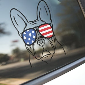 May include: A black and white outline of a French bulldog wearing sunglasses with an American flag design. The sunglasses are red, white, and blue.