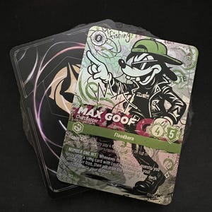 May include: Two trading cards are displayed. The front card features a cartoon character, Max Goof, in a green cap and sunglasses, pointing. The card has text including "Chart Topper" and "Floodborn". The back card has a black and white design.