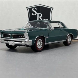 May include: A dark green model car with chrome accents and red-lined tires. The car has the word "GTO" on the front and a license plate that reads "GTO". The car is a classic model.