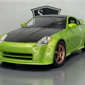 May include: A lime green Nissan 350Z scale model car featuring a black bonnet and roof, copper-coloured wheels, and clear headlights. The vehicle displays the Nissan logo on the front bumper and has a sleek, aerodynamic body design with side mirrors.