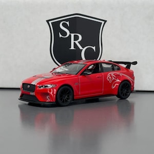Pode incluir: Um carro modelo vermelho com rodas pretas e um spoiler traseiro. O carro tem uma faixa branca no centro e um logotipo de jaguar na lateral. O fundo apresenta um logotipo em preto e branco.