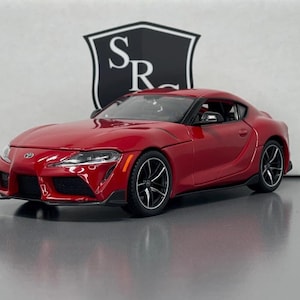 Könnte beinhalten: Ein rotes Toyota Supra Sportwagenmodell. Das Auto ist ein Modell im Maßstab 1:18 und verfügt über eine detaillierte Außengestaltung.