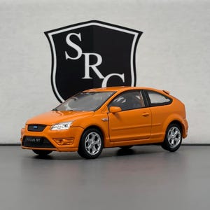 Könnte beinhalten: Orangefarbenes Ford Focus ST-Modellfahrzeug im Maßstab. Das Auto hat schwarze Verzierungen und schwarze Räder.