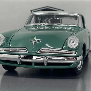 May include: A green vintage car with chrome detailing. The car features a classic design with rounded headlights and a prominent front bumper. The car's body is a deep green colour, and the chrome details add a touch of elegance. The car is a model of a Studebaker.