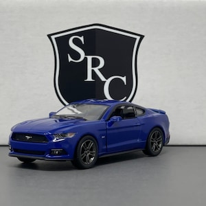 May include: A blue die-cast model car with black wheels. The car is a coupe with a sleek design. The background features a white surface with a black and white logo that reads "SRC".