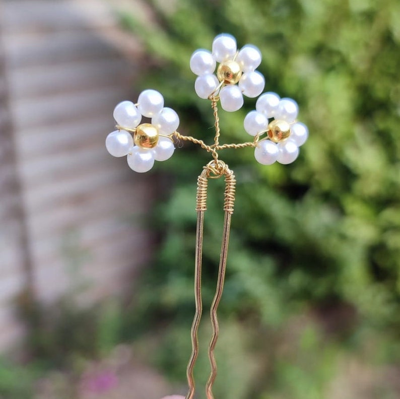 May include: A gold hair pin with three white pearl flower accents. Each flower has a gold center.