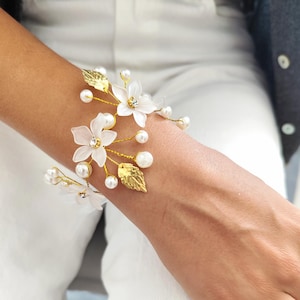May include: A delicate gold bracelet with white flowers and pearls. The bracelet features a floral design with small white flowers and gold leaves. The flowers have a pearl center and are accented with small gold beads.