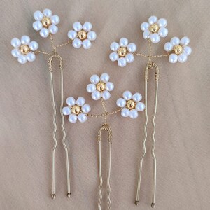 May include: Three gold hair clips with pearl and gold flower accents. Each clip has a different design and features multiple flowers.