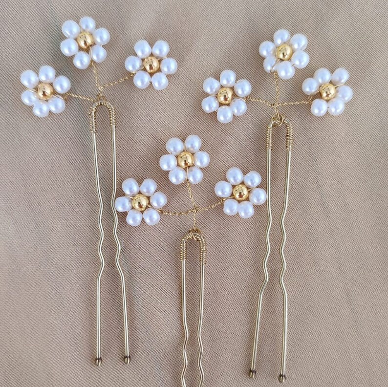 May include: Three gold hair clips with pearl and gold flower accents. Each clip has a different design and features multiple flowers.