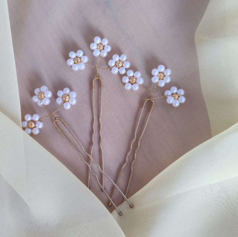 May include: Four gold hair pins with pearl flower accents. Each pin has a different number of flowers, ranging from one to four. The flowers are made of small white pearls arranged in a circular pattern.