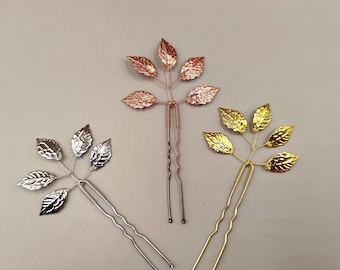 May include: Three gold hair clips with leaf designs. The leaves are in different shades of gold, silver, and rose gold.