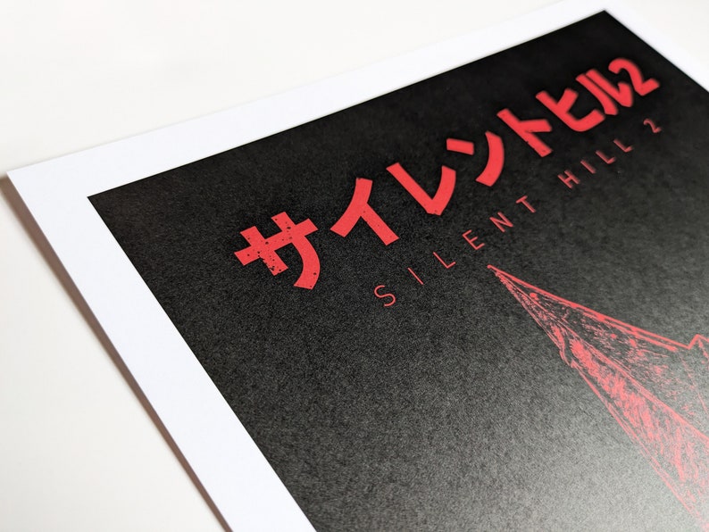 Silent Hill 2 Game Poster - Character set on a black background with a mixture of Japanese and English text in red. Available in A5, A4, A3 & A2. This close up photo shows the detail of the Japanese and English title text.