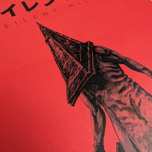 Silent Hill 2 Game Poster - Character set on a red background with a mixture of Japanese and English text in black. Available in A5, A4, A3 & A2. This close up photo shows the detail of the the main character.