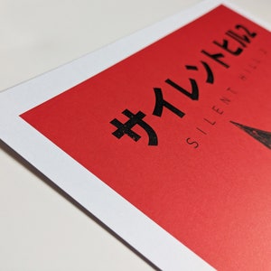 Silent Hill 2 Game Poster - Character set on a red background with a mixture of Japanese and English text in black. Available in A5, A4, A3 & A2. This close up photo shows the detail of the Japanese text.