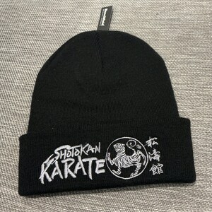 Peut inclure: Un bonnet noir avec un motif brodé blanc représentant les mots "Shotokan Karate" et un tigre. Le motif comprend également des caractères japonais.