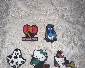 May include: A selection of Halloween-themed shoe charms. The charms feature a ghost, a heart with a figure, a character in a blue dress, and two Hello Kitty designs, one with Frankenstein's monster and the other riding a broom.