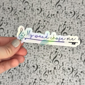 May include: A white sticker with a rainbow iridescent finish. The sticker features a treble clef and the text "My wand chose me".