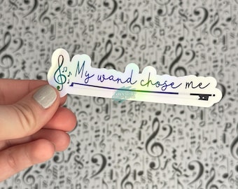 May include: A white sticker with a rainbow iridescent finish. The sticker features a treble clef and the text "My wand chose me".
