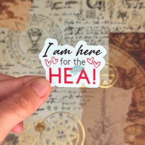 May include: A white sticker with the text "I am here for the HEA!" in black and red. The sticker has three small red hearts. The background is a collage of vintage paper and maps.