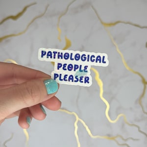 Könnte beinhalten: Ein weißer Aufkleber mit schimmerndem Glitzer und blauem Text, der "Pathological People Pleaser" lautet.