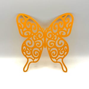 May include: A bright orange butterfly cutout featuring an intricate, openwork filigree pattern of swirling lines and curves. The design is symmetrical, with delicate, thin borders forming the shape of the wings and a central body section.