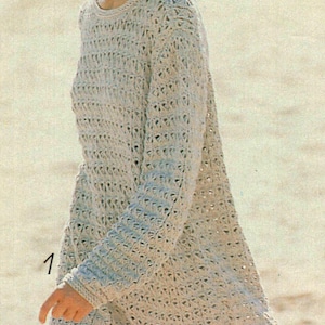 May include: A light beige, open-weave knit dress with long sleeves. The dress has a round neckline and a loose fit. The person in the image is wearing a straw hat. The number 1 is visible on the left side of the image.