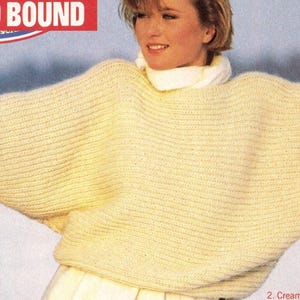May include: A woman wearing a cream-colored, oversized sweater with a high, white turtleneck. The sweater has wide sleeves and a ribbed texture. The text "OUTWARD BOUND" is visible at the top of the image.