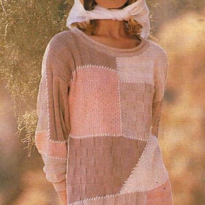 May include: A patchwork sweater dress in shades of pink, beige, and brown. The long-sleeved dress features a round neckline and a mix of textured and solid panels. A white scarf and a beige hat are also visible.