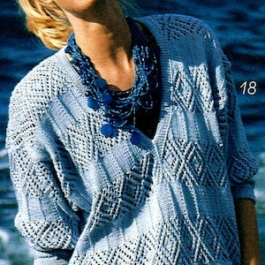 May include: Light blue knit sweater with a V-neck and diamond pattern. The sweater has long sleeves and is worn with a blue beaded necklace. The number "18" is visible on the right side of the image.