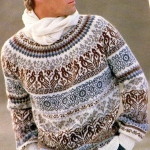 Könnte beinhalten: Ein gemusterter Pullover in Braun-, Blau- und Weißtönen. Der Pullover hat einen Rundhalsausschnitt und lange Ärmel mit einem detaillierten geometrischen Design. Ein weißer Schal wird ebenfalls getragen.