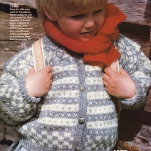 Può includere: Un bambino indossa un cardigan a fantasia grigio e bianco con bottoni argentati e una sciarpa rossa. Il cardigan presenta un design a righe e geometrico. Il numero 10 è visibile in basso a destra.