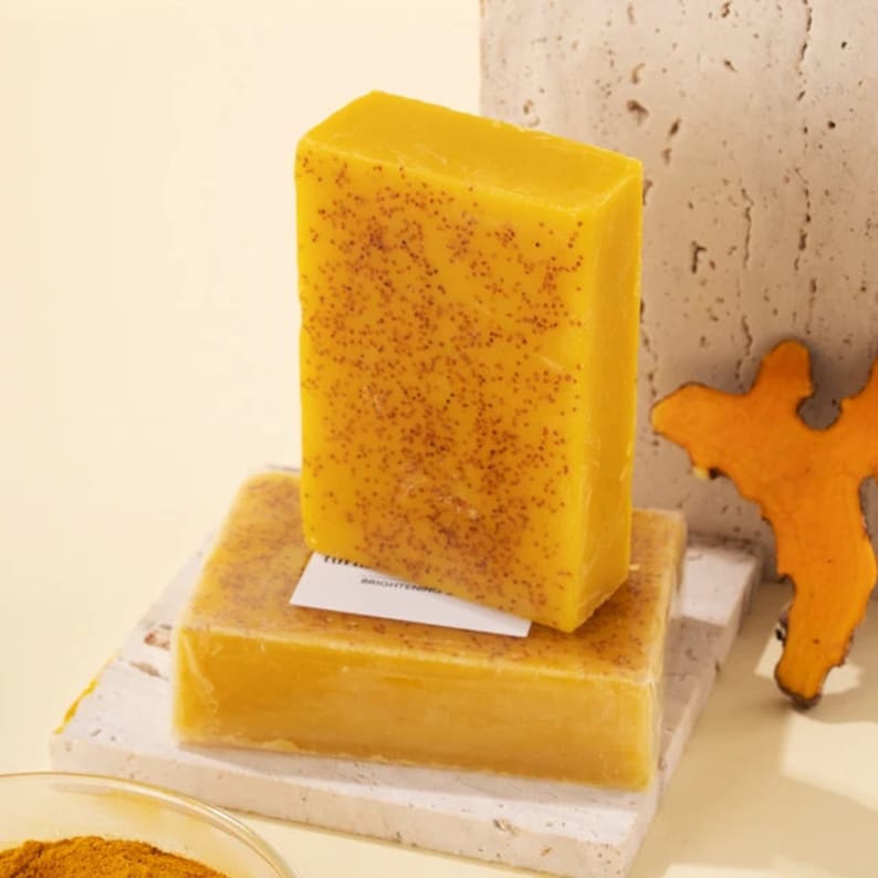 Puede incluir: Dos barras de jab&oacute;n amarillo con textura moteada. La barra superior es ligeramente m&aacute;s grande que la barra inferior. Las barras est&aacute;n sobre una superficie blanca.