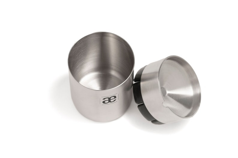 May include: A stainless steel coffee grinder with a black rubber base and a removable lid. The grinder has a logo that says "ae" on the side.