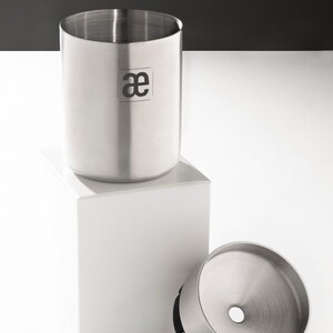 May include: A stainless steel coffee grinder with a removable funnel and a black rubber base. The grinder has a logo that says "ae" on the side.