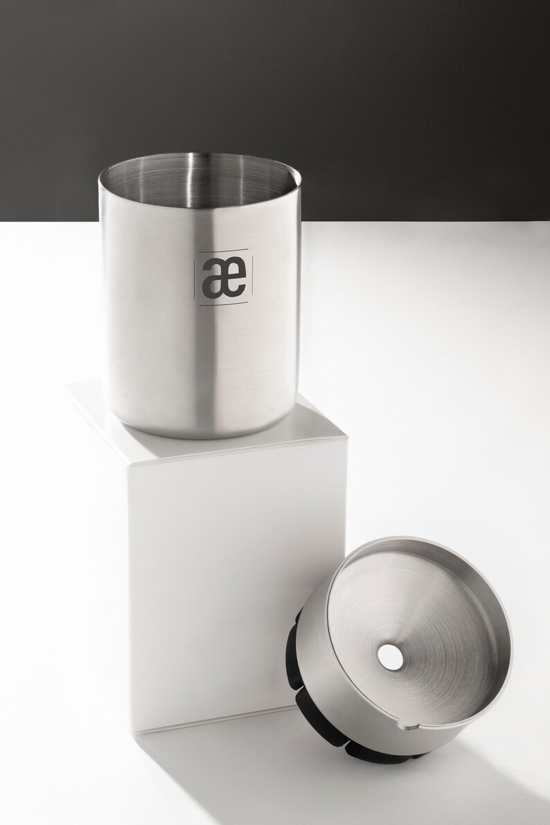 May include: A stainless steel coffee grinder with a removable funnel and a black rubber base. The grinder has a logo that says "ae" on the side.