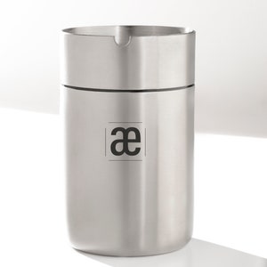 May include: A silver stainless steel container with a black logo that says "ae" inside a square.
